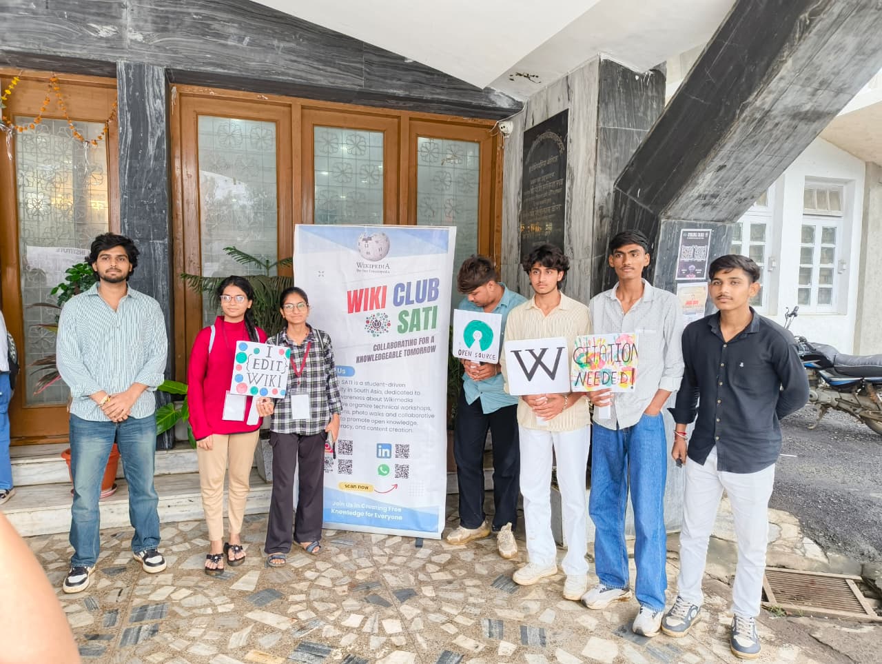 The Wiki Club at SATI (Samrat Ashok Technological Institute) hosts an interactive outreach event featuring a standee designed to promote awareness of open-source principles and the role of collaborative knowledge-sharing platforms such as Wikipedia. The standee is accompanied by cutouts of key concepts related to open-source software and community-driven editing. This initiative encourages students and faculty to engage with open-source initiatives by posing for photographs, thereby contributing to a broader dialogue on the importance of open access to information and the power of collective contribution. Through this visual engagement, the Wiki Club aims to foster greater involvement in the global open-source movement. concerning Multimodal Prompt Engineering in Gemini: Dissecting Latent Space Dynamics and Semantic Control in Generative Image Editing